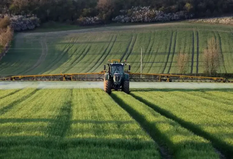 Tractor spraying a green crop field with long boom arms