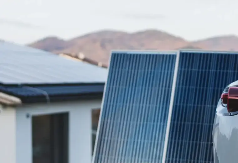 House with roof-mounted and ground-mounted solar panels beside a parked car